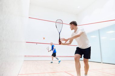 İki genç, konsantre ve sportif adam, squash kortunda beraber squash oynayan arkadaşlar. Egzersiz ve boş zaman. Spor anlayışı, hobi, sağlıklı ve aktif yaşam tarzı, oyun, spor salonu, reklam