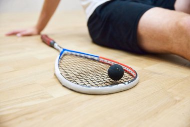 Erkek bacakları ve raketle top. Adam squash sahasında squash antrenmanından sonra yerde oturup dinleniyor. Spor anlayışı, hobi, sağlıklı ve aktif yaşam tarzı, oyun, spor salonu, reklam