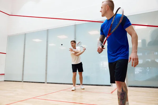Two young men, friends playing squash together on squash court. Competition and leisure. Concept of sport, hobby, healthy and active lifestyle, game, gym, ad