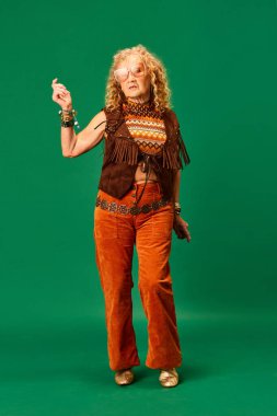 Hippi tarzı. Yeşil stüdyo arka planında duran şık kıyafetler ve aksesuarlarla abartılı bir son sınıf kadını. İnsan duyguları, moda, yaşlı insanlar, yaşam tarzı, yaratıcılık kavramı. Ad