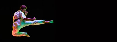 Genç bir adamın dinamik görüntüsü, hareketli bir karate atleti, neon ışıklarıyla siyah stüdyonun arka planında eğitim görüyor. Dövüş sanatları kavramı, dövüş sporu, enerji, güç, sağlık. Pankart. İlan için alanı kopyala