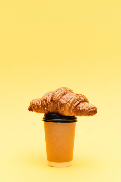 Freshly baked, crispy croissant on coffee cup to go over yellow background. Take away food. Concept of food, bakery, breakfast ideas, taste, freshness. Poser. Copy space for ad