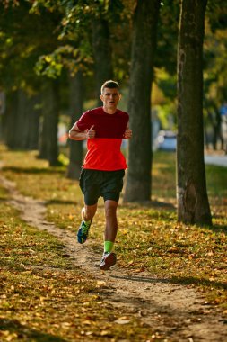Genç kaslı adamın dinamik görüntüsü, hareket halindeki sporcu sabahın erken saatlerinde parkta koşuyor, dışarıda antrenman yapıyor. Spor anlayışı, aktif ve sağlıklı yaşam tarzı, rekabet, dinamik, maraton