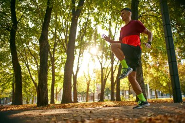 Atletik genç adam, koşan bir atlet. Eğitim, güneşli savaş günlerinde şehir parkında farklı egzersizler yapmak. Spor anlayışı, aktif ve sağlıklı yaşam tarzı, rekabet, dinamik, maraton