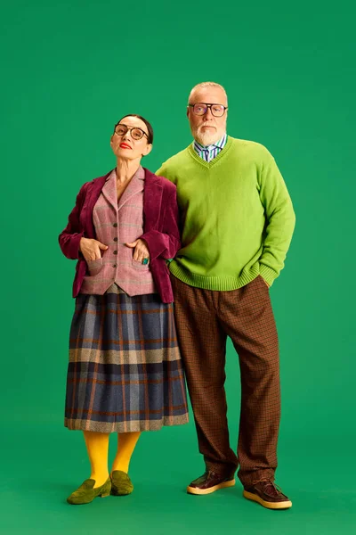 Beautiful grandparent. Elegant senior woman and man in cozy outfits posing against green studio background. Concept of beauty and fashion, relationship, modern style, age