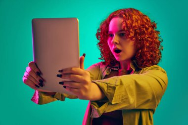 Kıvırcık saçlı, duygusal olarak tablete bakan genç bir kız. Şaşkınlık, şok. İnsan duyguları, yaşam tarzı, gençlik, yüz ifadesi kavramı. Ad