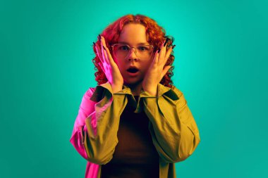 Kızıl saçlı, kıvırcık saçlı genç bir kız. Şok olmuş yüzüyle neon ışıkta siyan arka planda duruyor. Şaşırmış görünüyorsun. İnsan duyguları, yaşam tarzı, gençlik, yüz ifadesi kavramı. Ad