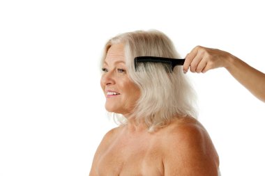 Saç bakımı, tedavi. Beyaz stüdyo geçmişine bakarak saçlarına özen gösteren gülümseyen son sınıf öğrencisi kadın. Saç fırçalamak. Doğal güzellik kavramı, yaşlanma süreci, yaşlı güzellik, kozmetoloji, cilt bakımı