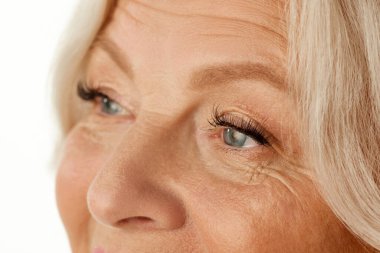 Yaşlı bir kadının yüzüne yakın çekim, maskaralı gözler. Güzel buruşuk surat. Doğal görünüş ve kendine dikkat. Vizyon. Doğal güzellik kavramı, yaşlanma süreci, yaşlı güzellik, kozmetoloji, cilt bakımı