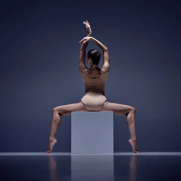 情熱を持って エレガントなバレリーナ ブルースタジオの背景に対して立方体にポーズベージュのボディスーツの若い女性 クラシックダンス アート グレース インスピレーションの概念 — ストック写真