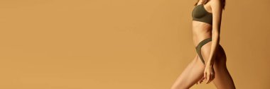 Kaslı, formda, sağlıklı bir kadın vücudu, göbek. Pamuklu iç çamaşırlarıyla açık kahverengi stüdyo arka planına karşı duran bir model. Doğal güzellik kavramı, vücut ve cilt bakımı, sağlık, spor
