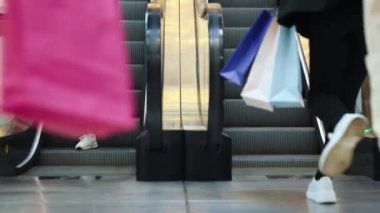 İnsanlar alışveriş merkezindeki yürüyen merdivenlerde ilerliyorlar. Bir sürü çanta taşıyorum, alışverişe gidiyorum. Büyük satışlar. Bir sürü insan mağazalara gidiyor. Alışveriş anlayışı, Kara Cuma, alışveriş merkezi, boş zaman.
