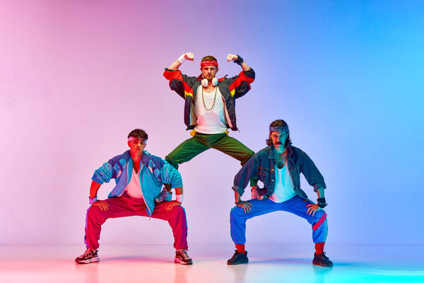 Team. Friends, tree men in colorful retro sportswear standing in pyramid pose against gradient pink blue background in neon light. Concept of sportive and active lifestyle, humor, retro style. Ad