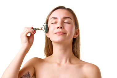 Güzel genç kız cildine özen gösteriyor, beyaz stüdyo arka planında izole edilmiş patenlerle yüz masajı yapıyor. Kaldırma etkisi. Doğal güzellik kavramı, cilt bakımı, kozmetik ve kozmetik.