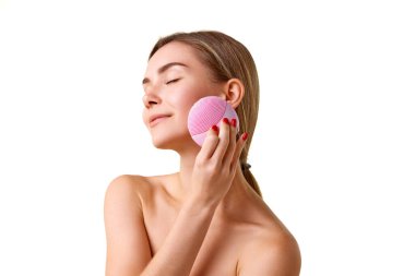 Derin yüz temizleme için silikon fırça kullanan iyi korunmuş genç bir kız. Beyaz stüdyo arka planında izole edilmiş. Doğal güzellik kavramı, cilt bakımı, kozmetik ve kozmetik.