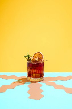Sarı arka planda bir dilim kuru portakal ve biberiye ile süslenmiş taze, lezzetli Negroni kokteyli. İçki, parti, tatil, bar, karışım kavramı. Poster. İlan için alanı kopyala