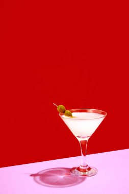 Geleneksel orijinal içki. Kırmızı arka planda izole edilmiş zeytinlerle süslenmiş martini bardağı. Kutlama. İçki, parti, tatil, bar, karışım kavramı. Poster. İlan için alanı kopyala