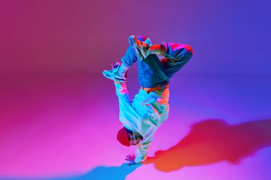 Hareketli şık spor kıyafetleri içindeki adam, dans eden break dans, neon ışıklarıyla izole edilmiş gradyan stüdyo arkaplanı. Çağdaş dans kavramı, sokak tarzı, moda, hobi, gençlik. Ad