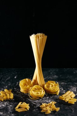 Farklı İtalyan makarnalarının kompozisyonu siyah masa üzerinde un ile. Penne, fusilli, rigatoni, farfalle, spagetti, fettuccine. İtalyan yemeği, yemek, tat, menü kavramı. İlan için poster
