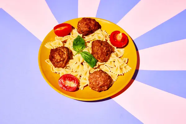 Top view of plate with delicious pasta, farfalle with meatballs, tomato and basil over pastel background. Concept of Italian food, cuisine, taste, cooking, menu. Pop art. Poster, ad