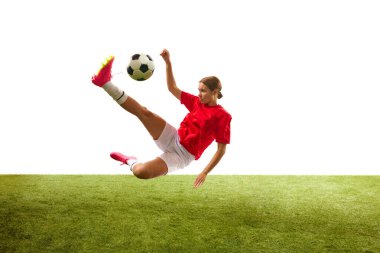 Genç bir kadın, hareketli bir bayan futbolcu, bacağıyla topa vuruyor ve beyaz arka planda çimlere gömülüp düşüyor. Spor, rekabet, aksiyon, başarı, kazanma kavramı. İlan için alanı kopyala