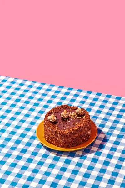 Chocolate delicious cake on plate on blue checkered tablecloth over pink background. Concept of food, desserts, birthday celebration, party, bakery. Pop art style. Copy space for ad. Poster