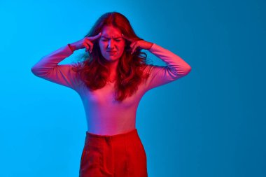 Genç kız parmaklarını kafasında tutuyor, baş ağrısı çekiyor, parlak ışıkta mavi stüdyonun arka planına karşı düşüncelerden muzdarip. Gençlik kavramı, insan duyguları, yüz ifadesi, yaşam tarzı