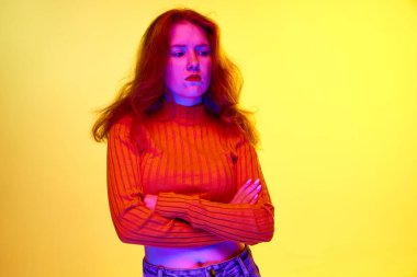 Gücenmiş yüz. Mutsuz, nahoş bir yüzü olan genç bir kız sarı stüdyo arka planına karşı neon ışıkta duruyor. Gençlik kavramı, insan duyguları, yüz ifadesi, yaşam tarzı