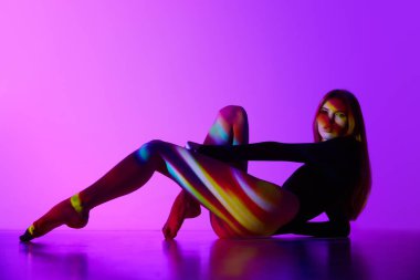 Bedeninde renkli neon ışıkları yansıması olan, mor arka planda poz veren seksi, güzel bir genç kız. Modern sanat, güzellik, tarz, fütürizm ve siber punk, yaratıcılık kavramı