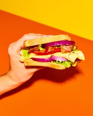 Izgara ekmek, jambon, marul, peynir, domates, soğan ve sarı turuncu arka planda avokado ile nefis sandviç tutan bir kadın. Yemek, tat, kahvaltı kavramı. Tamamlayıcı renkler. Poster, reklam