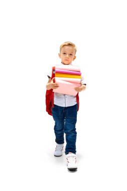 Sırt çantası ve yığınla kitabı olan yakışıklı çocuk beyaz arka planla okula gidiyor. Çocuk gibi çalış ve öğren. Anaokulu. Online eğitim. Çocukluk kavramı, Uluslararası Bilgi Günü. Boşluğu kopyala, ad.