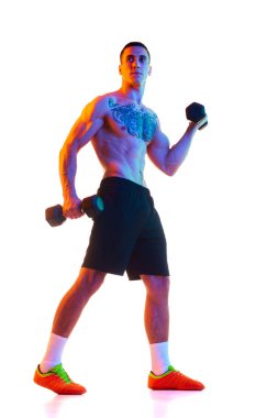 Güçlü, kaslı vücut eğitimi almış, dambılları beyaz stüdyo arka planına dayanan üstsüz genç bir adam. Spor anlayışı, aktif ve sağlıklı yaşam tarzı, vücut, fitness