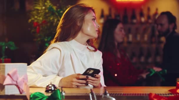 年轻优雅的女人坐在酒吧里 看着电话 等待朋友或男朋友的到来 寂寞的约会 庆祝会 放松的概念 — 图库视频影像