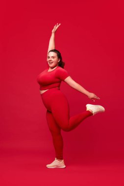 Mutlu, gülümseyen, kilolu genç bir kadın. Kırmızı stüdyo geçmişine karşı vücut şekli eğitimi almış. Spor anlayışı, vücut pozitifliği, kilo kaybı, vücut ve sağlık hizmetleri