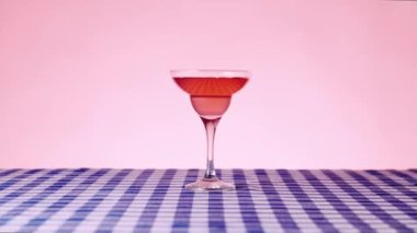 Pembe arka planda damalı masa örtüsü üzerine tatlı Manhattan kokteyli. Dekorasyon için kiraz konyağı koyuyorum. Kokteyl kavramı, alkol içeceği, bar, tat, menü, pop sanat tarzı.