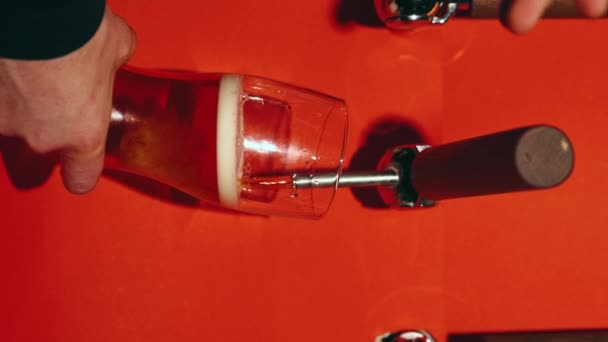 バーテンダーはゆっくりと赤い背景に対してガラスに美味しいラガー泡立ったビールを注いでいます バブルのクローズアップ 飲み物 醸造所 飲み物質のコンセプト 垂直レイアウト — ストック動画
