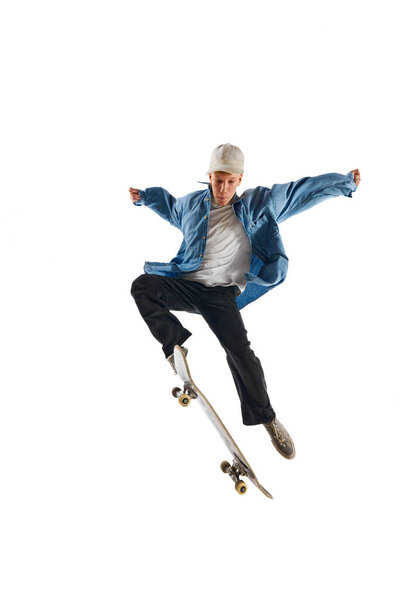 Sportive, active young man in casual clothes in motion, training with skateboard, doing stunts isolated over white background. Concept of professional sport, competition, training, action.