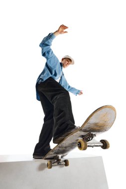 Alttaki görüntüde, hareketli, eğitimli, beyaz arka planda izole edilmiş kaykay üzerinde dublörlük yapan genç bir çocuk görülüyor. Profesyonel spor kavramı, rekabet, eğitim, eylem.