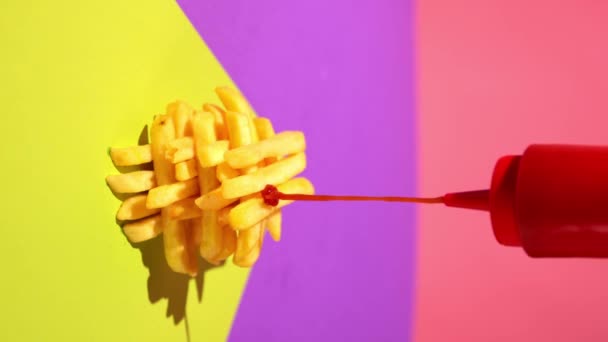 番茄酱在美味的炸土豆片上压榨 薯条在五颜六色的背景上压榨 增加食物的味道 垃圾食品的概念 互补的颜色 — 图库视频影像