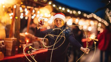 Kış fuarında rahat bir akşam sokağında duran mutlu genç adam Noel 'i kutluyor, elinde lamba ve bardakla sıcak şarap tutuyor. Kış tatili, Noel, gelenekler, adil, mutluluk kavramı
