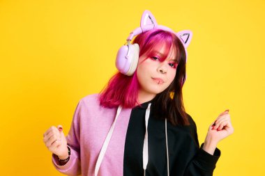 Parlak makyajlı, piercingli ve saçları iki renge boyanmış kulaklıkla müzik dinleyen parlak sarı stüdyo geçmişi olan genç bir kız. Gençlik kavramı, kendini ifade etme, moda, duygular