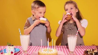 Mutlu, neşeli sevimli çocuklar, erkek ve kız doğum gününü kutluyor, sarı arka planda kek yiyorlar. Olumlu duygular. Çocukluk kavramı, doğum günü kutlaması, aile, eğlence, yemek
