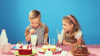 Mutlu, neşeli güzel çocuklar, erkek ve kız doğum gününü kutluyorlar, mavi arka planda milkshake içiyorlar. Çocukluk kavramı, doğum günü kutlaması, aile, eğlence, yemek