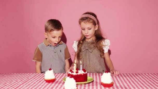 小さな男の子と女の子 兄と妹は誕生日のケーキでテーブルに立って ピンクの背景にショックを与えました 子供の頃の概念 誕生日のお祝い 楽しみ 食べ物 — ストック動画