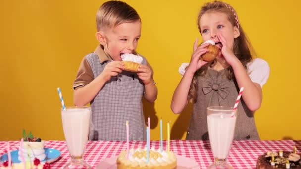 誕生日を祝い 黄色い背景にケーキを食べる 陽気で愛らしい子供たち 少年少女 ポジティブな感情 子供の頃の概念 誕生日のお祝い 楽しみ 食べ物 — ストック動画