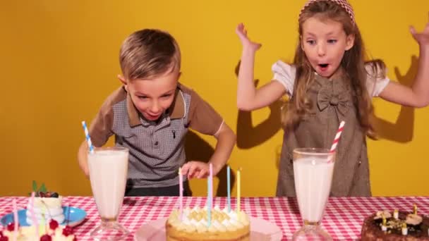 ハッピー かわいい小さな男の子 男の子 少女は黄色の背景に対してケーキでテーブルの近くにジャンプします 子供の頃の概念 誕生日のお祝い 楽しみ 食べ物 — ストック動画