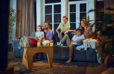 Mutlu gülümseyen bir aile, aileleri akşamları kanepede televizyon izleyen çocuklar. Pozitif duygular, sıcak zamanlar. Aile kavramı, boş zaman, rahatlama, çocukluk ve ebeveynlik