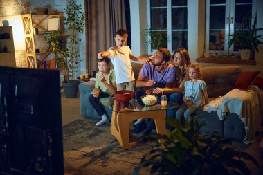 Aile zamanı. Erkek, kadın ve çocuklar akşam evde birlikte televizyon izliyorlar. Çocuk anne ve babasıyla film sahnesini tartışıyor. Aile kavramı, boş zaman, rahatlama, çocukluk ve ebeveynlik