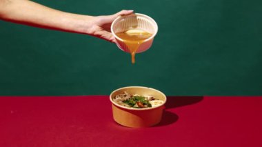 Lezzetli ramen yapıyorum. Yeşil arka planda erişte, sebze ve baharatla çorba döken bir kadın. Asya yemeği, lezzet, aşçılık, pop sanat tarzı, malzemeler.