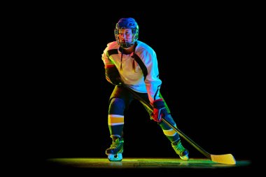Genç bir kız, üniformalı bir hokey oyuncusu ve kask eğitimi almış, neon ışıkta siyah bir stüdyonun arka planında duruyor. Profesyonel spor kavramı, rekabet, oyun, eylem, hobi